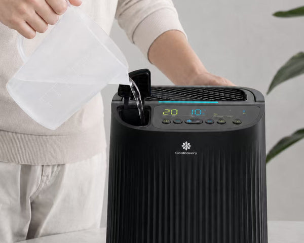 Person cleaning a black air purifier with a white cloth on a light background
