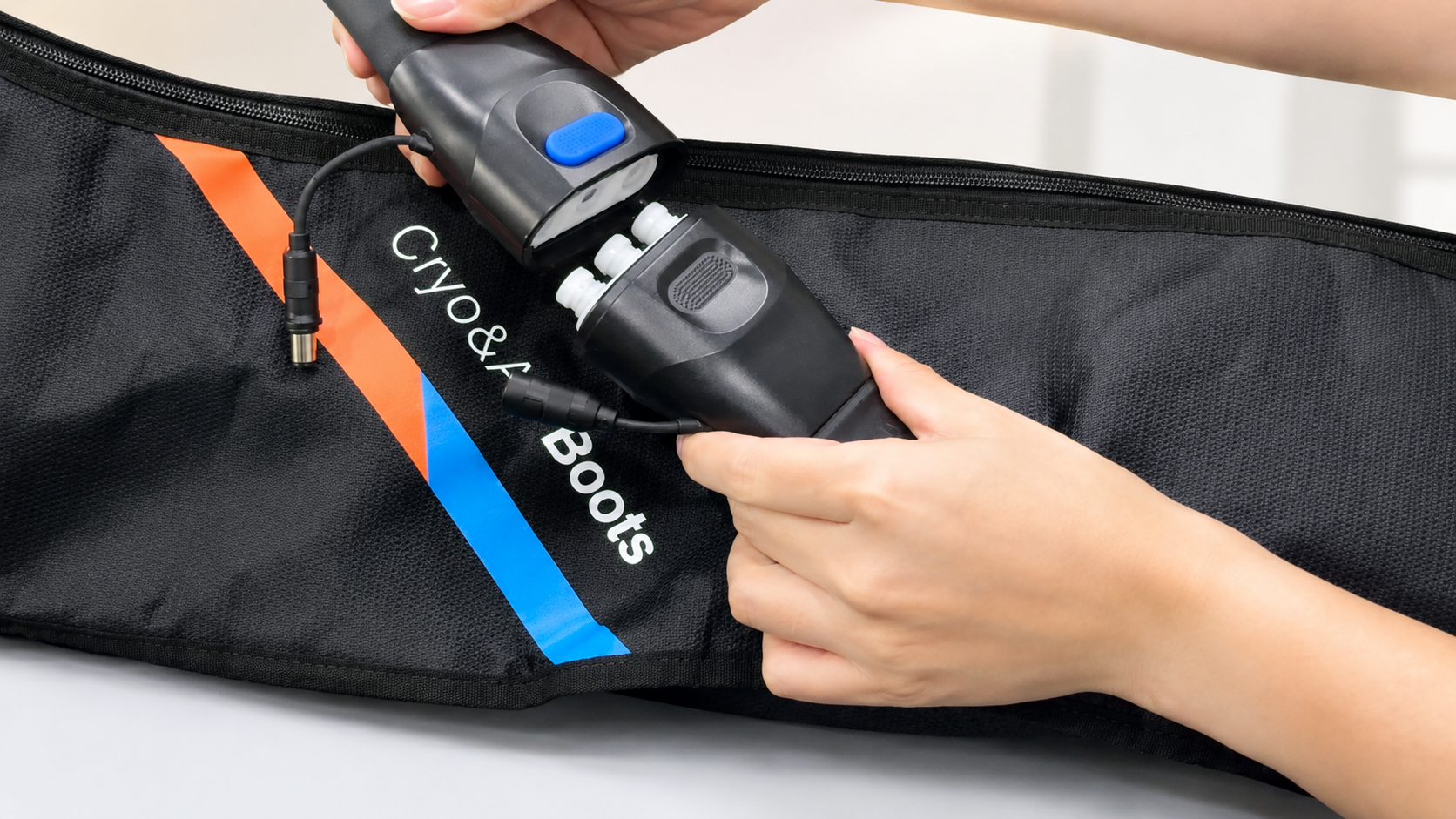A person's hands holding a black Cryo & Boots cryotherapy tool over a black insulated boot bag with orange and blue accents.