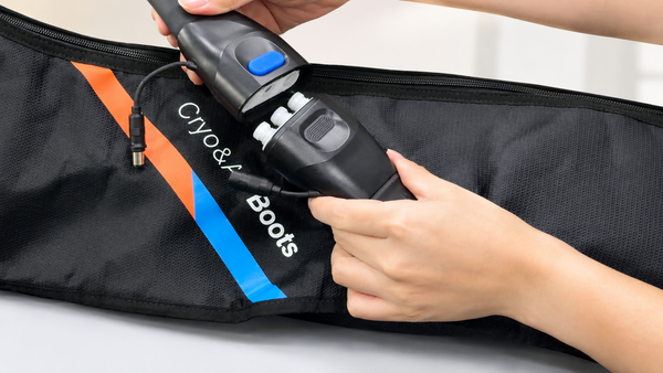 A person's hands holding a black Cryo & Boots cryotherapy tool over a black insulated boot bag with orange and blue accents.